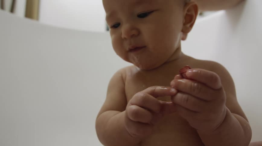 Child sits in tub eating fruit as mother watches