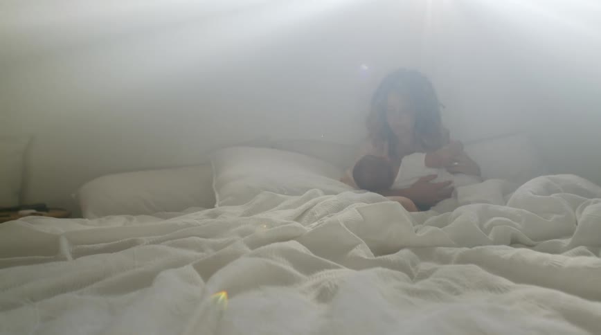 A woman cradles a baby while sitting up in bed