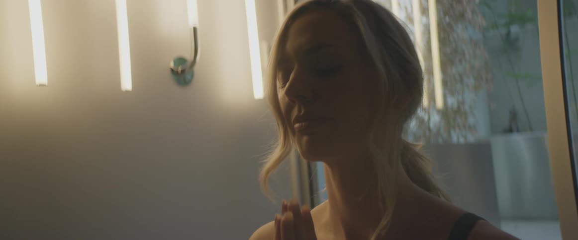 Blonde woman with black sports bra practices yoga in room