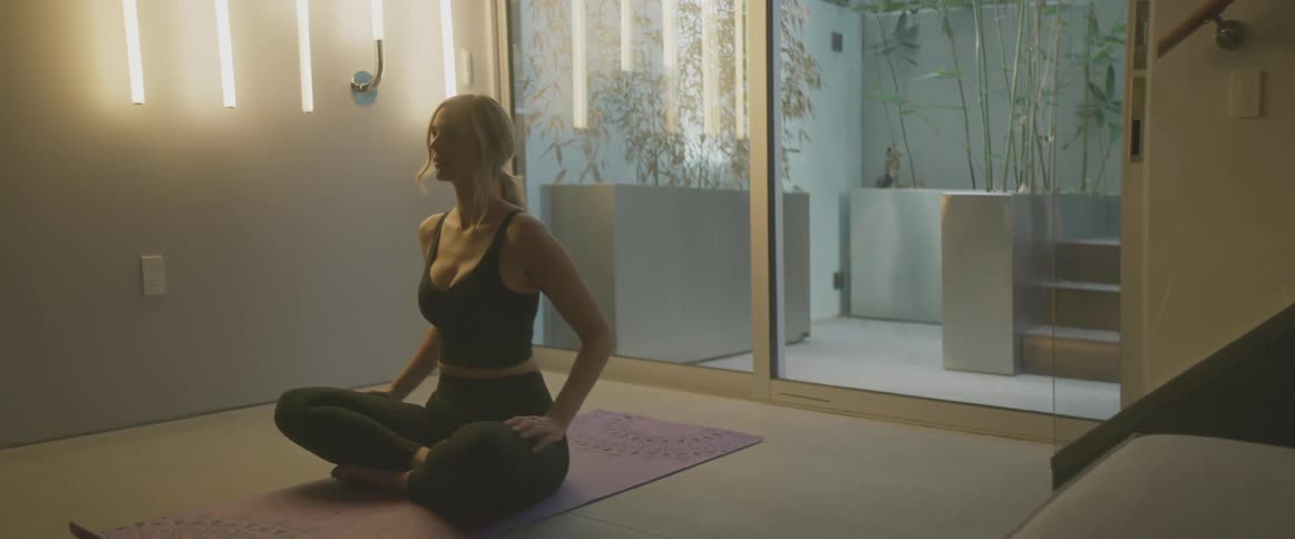 A woman at home sits on a yoga mat and stretches