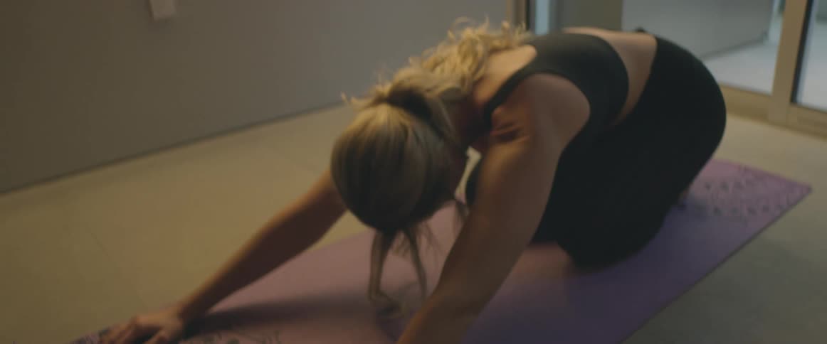 A woman stretches her back while doing yoga on the floor in her living room