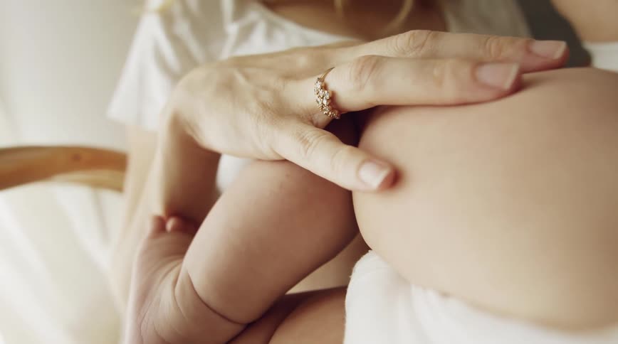 Mom sitting with her hand on babys chubby leg as she breast feeds