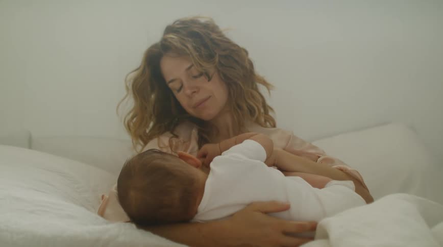 A mother cradles her baby in bed