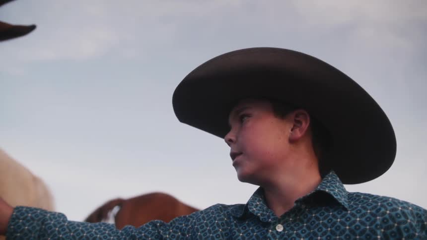 Young cowboy reaching towards a horse in front of him