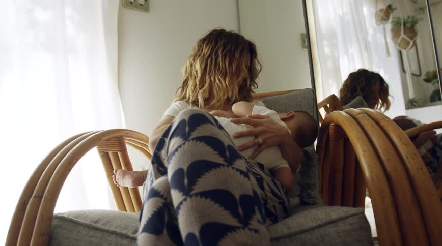 Mother sits in chair near window holding baby to her chest
