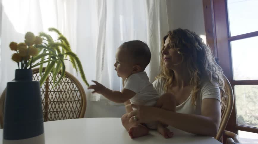 Mother holds child and pulls them back as child holds for plants in vase