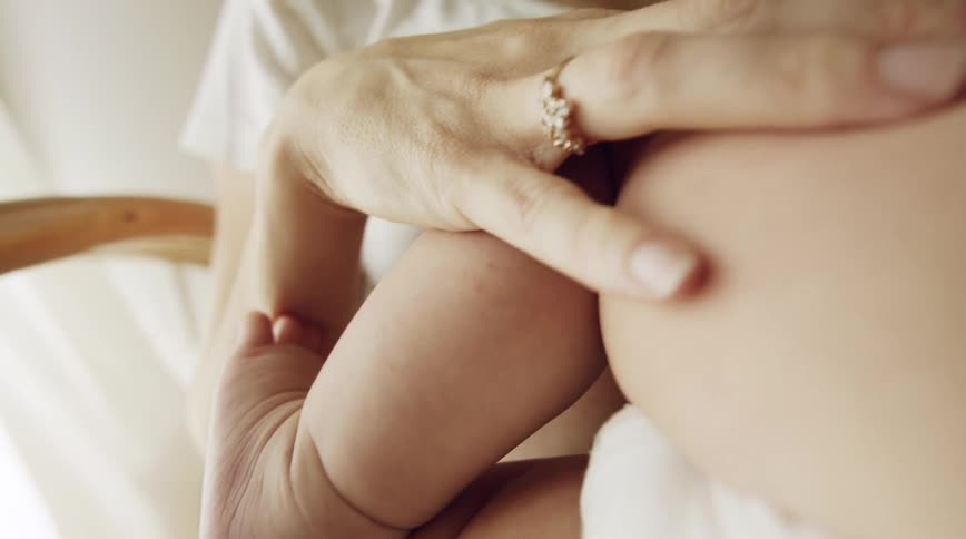Mom holds babys chubby leg as she breast feeds him