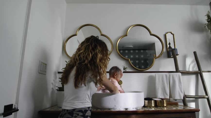A woman bathes her baby in a sink at home