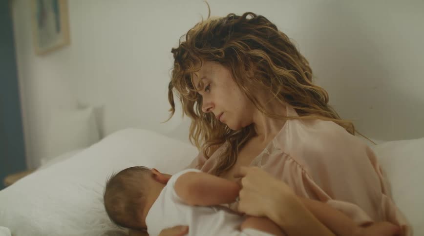 Mother with brown wavy hair breastfeeds baby in room