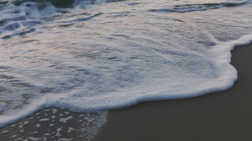Ocean waves wash into a sandy beach during the day