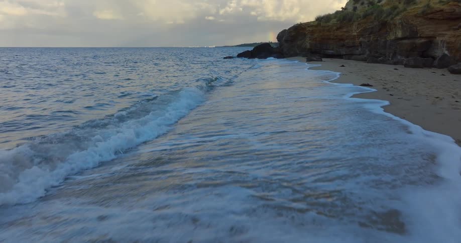 Waves roll in over a beach along the coast under a cloudy sky
