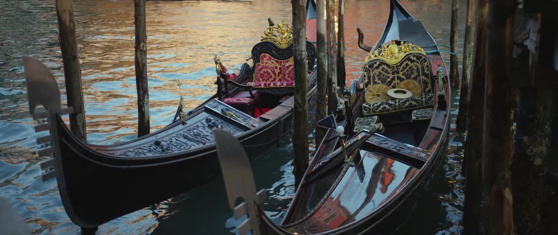 Two richly decorated gondolas rock in the water near the dock in Venice, Italy