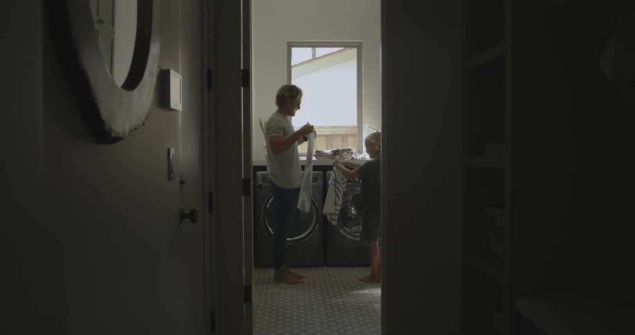 A father and young child folding laundry in front of a washer and dryer