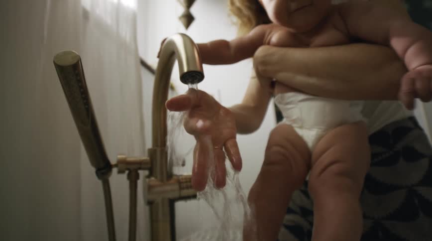 A mother splashing water from a kitchen faucet onto her babys legs