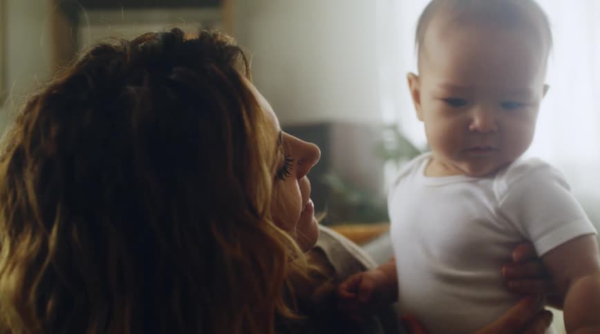Mom sitting at home holding her baby on her lap smiling at him