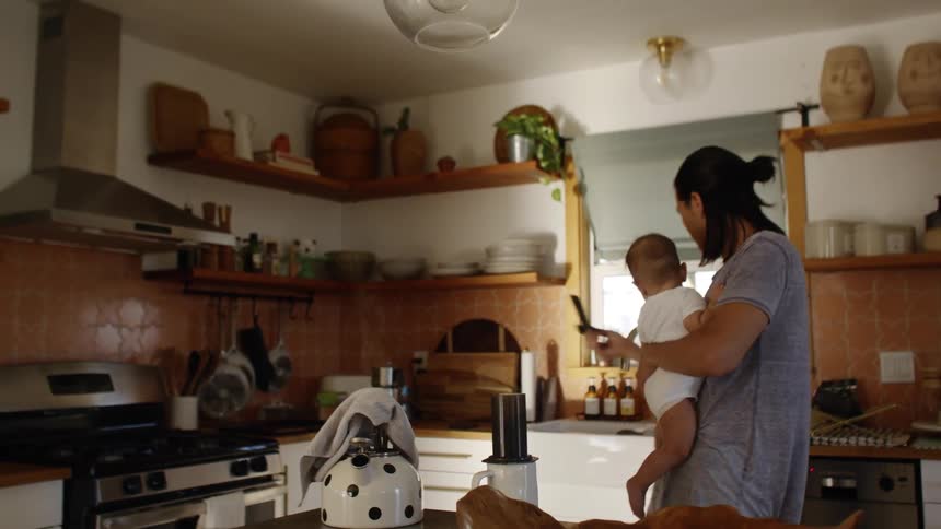 A man at home prepares a drink while he holds his baby