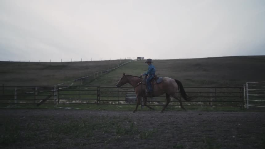 A person is riding a horse near a fence on a ranch