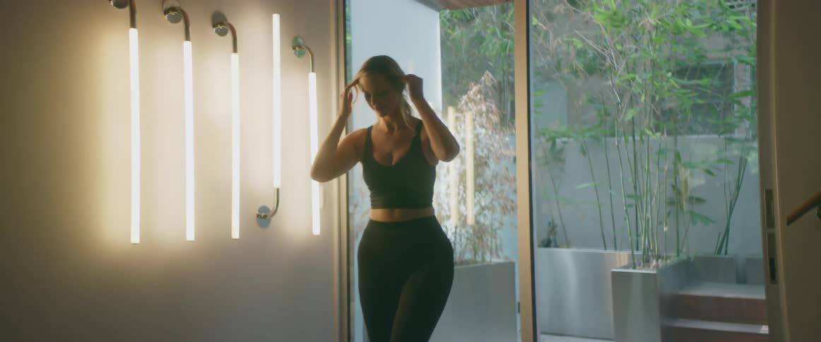 A woman wearing fitness attire unrolls a yoga mat inside of her home