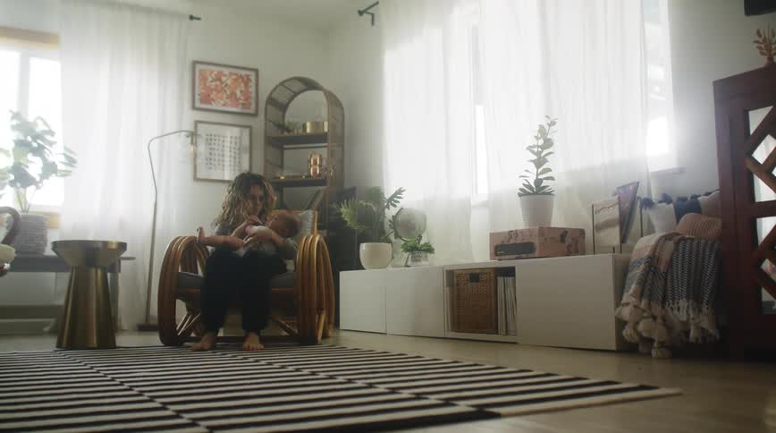 A woman cradles a baby while sitting in a chair indoors during the day