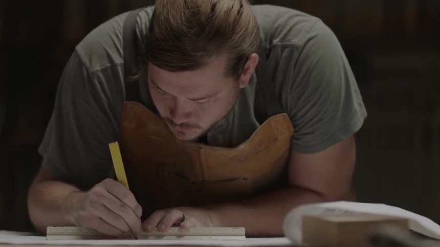 A man in a brown apron sketches on a work table