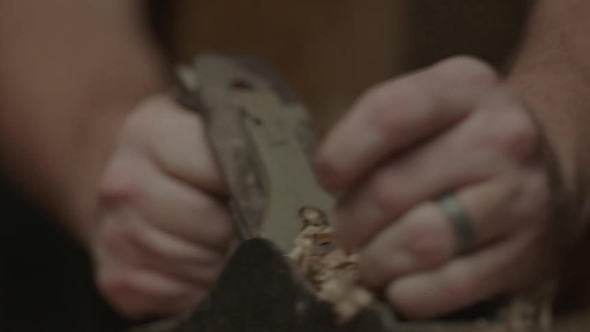 A person is shaving wood with a tool