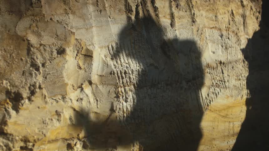 Two people cast shadow on rock wall one reaching up to adjust their hat