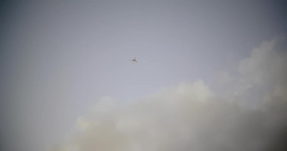 Airliner flies across cloudy pale gray blue sky