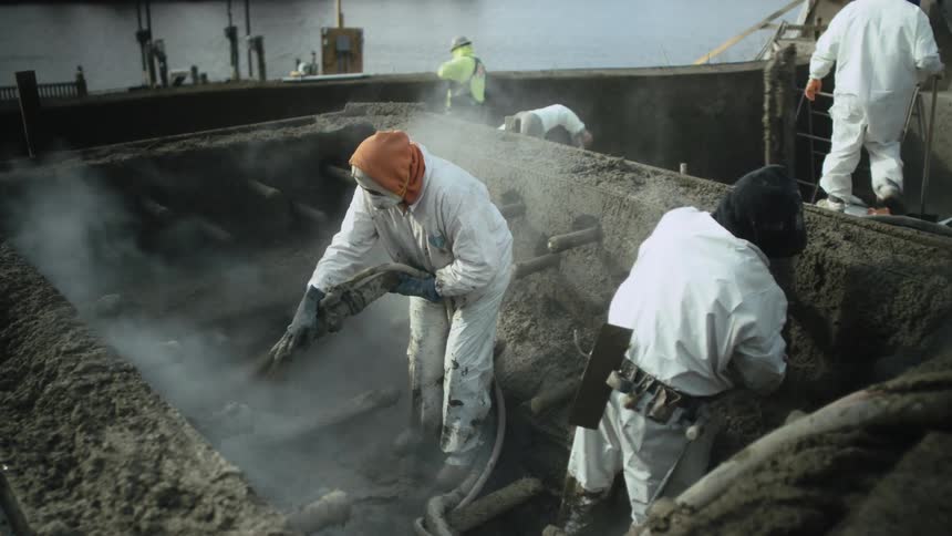Workers wearing protective gear work at construction site near water
