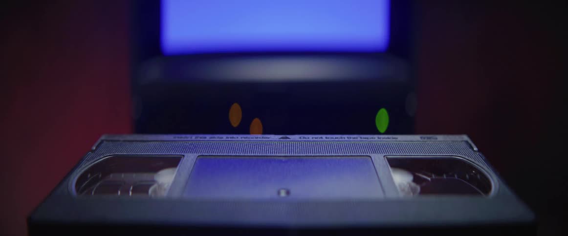 A vhs cassette tape slowly glides through the air towards a television