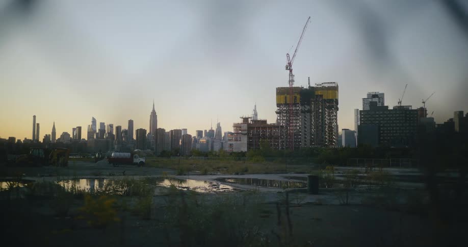 Construction cranes work on buildings with red sky backed city in the background