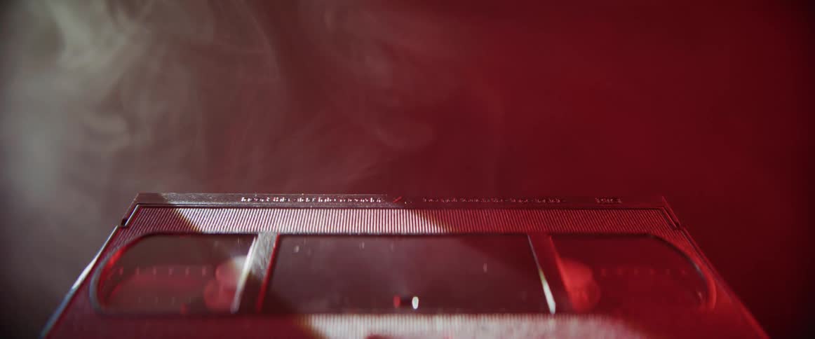 Red light flashes near a vcr tape as smoke rises around the tape