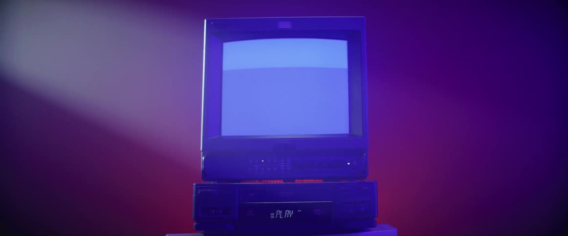 Static on the screen of a vintage televisor atop a vcr or dvd player inside a room under a spotlight