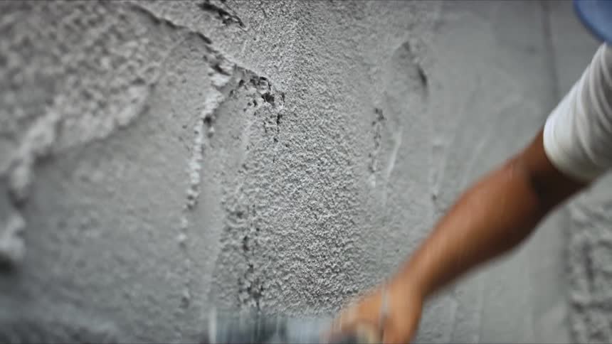 Worker uses steel plastering trowel to apply gray plaster over a wall