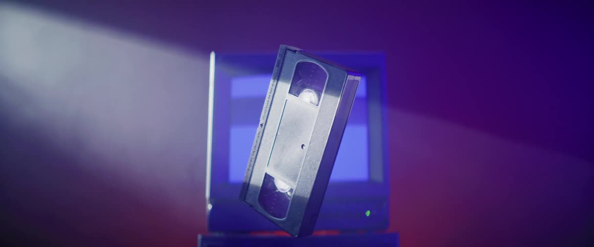 A vhs tape floating in a beam of light in front of a vintage computer