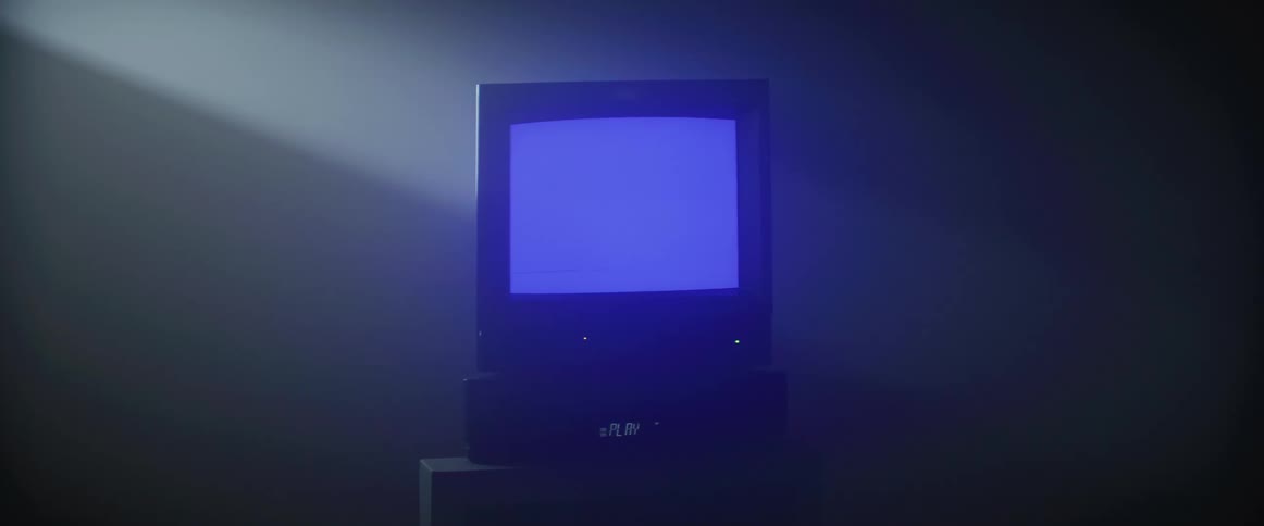 A television is sitting on top of a video player with the words play and a red light is shining on the wall