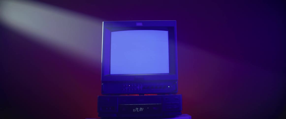Static on the screen of a vintage televisor atop a vcr or dvd player inside a room under a spotlight