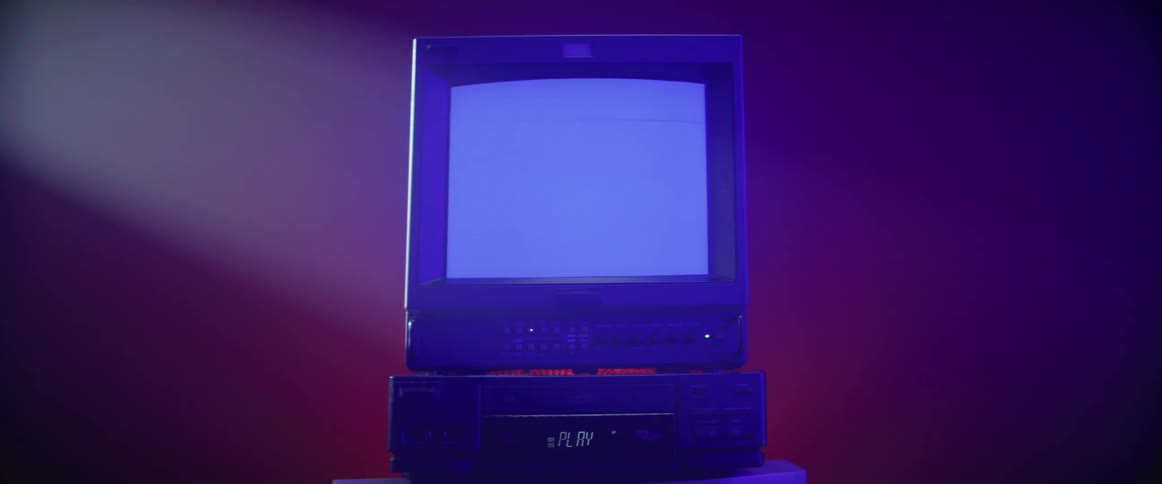A portable television is sitting on top of a video player and a red light is shining on the wall