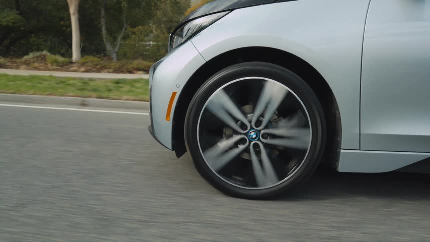 A newer model of compact electric car drives slowly down a paved street