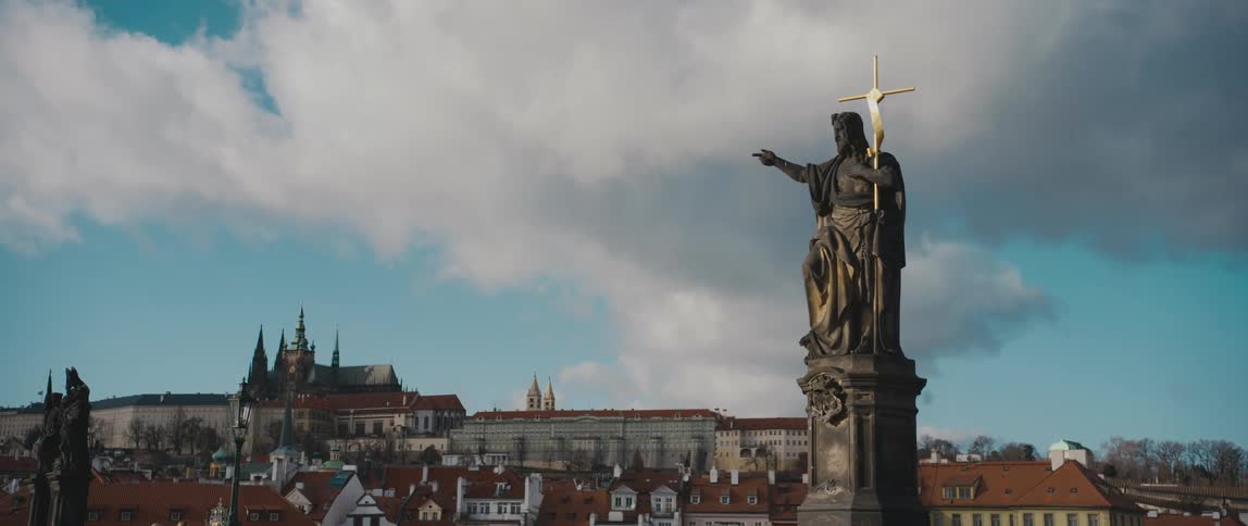 A view Prague, Czech Republic from Charles Bridge with Statue of Saint John the Baptist holding a golden cross in the foreground.