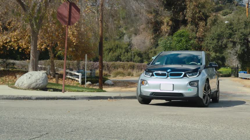 A person drives a small and stylish electric vehicle along a paved residential street