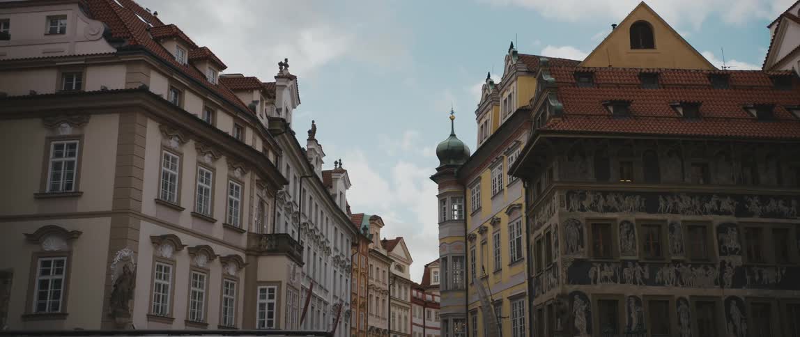 Buildings and gothic architecture of Old Town Square in Prague, including a glimpse of a green spire of Hussite St Nicholas Church in the background