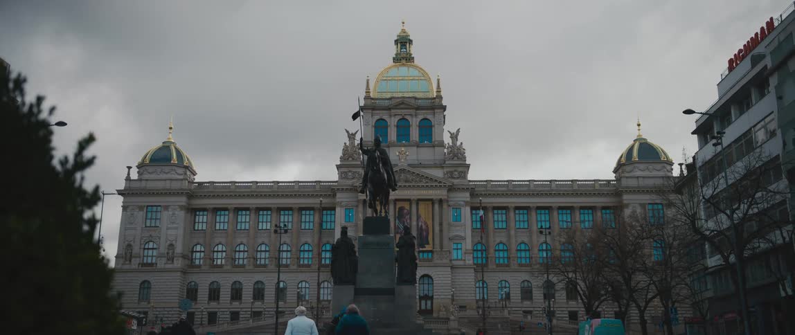 Pedestrians walking in front of an equestrian statue in front of a classical building