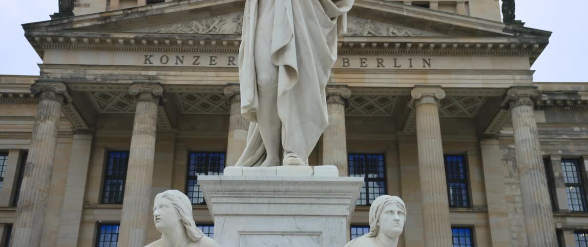 View of the Konzerthaus concert hall in Berlin with the Schiller monument in the foreground including statue of poet, philosopher, and historian Friedrich Schiller flanked at his feet by Allegory of Lyric Poetry (L) and Allegory of Tragedy (R).