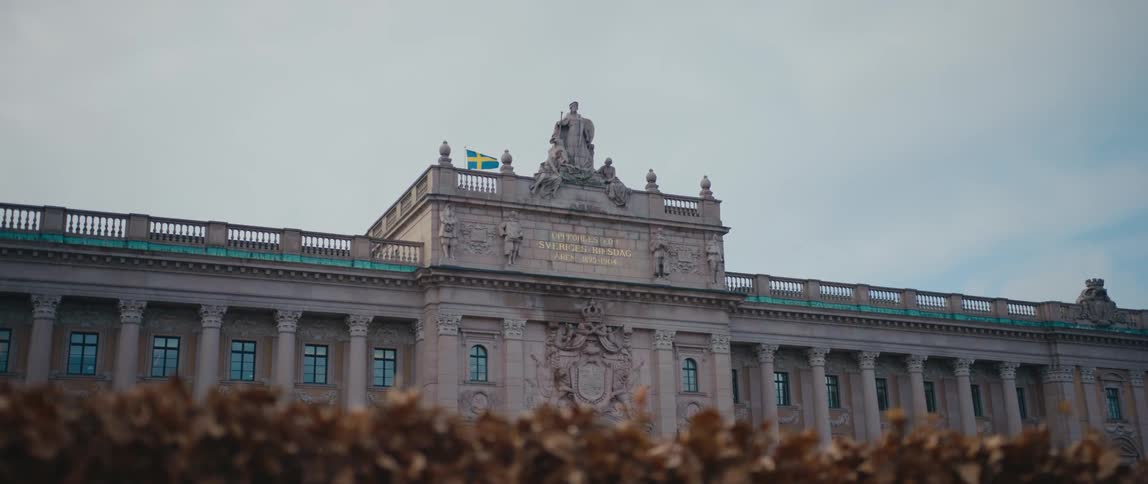 Blue and yellow flag flies next to a statue on top of a building under a cloudy blue sky