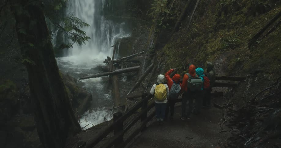 A group of hikers observe a waterfall in the wilderness on a rainy day