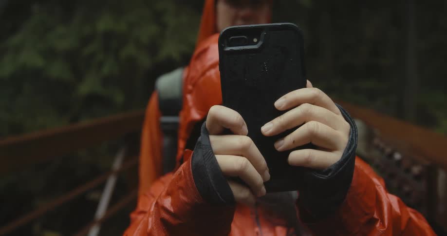 A woman taking video with a smartphone outside during a rainstorm
