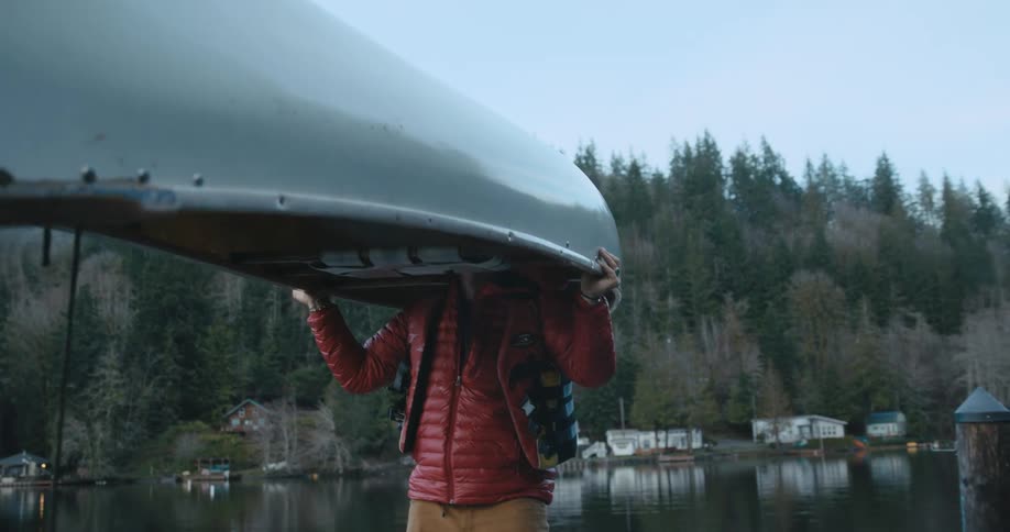 A man balancing a canoe on his shoulders next to a lake
