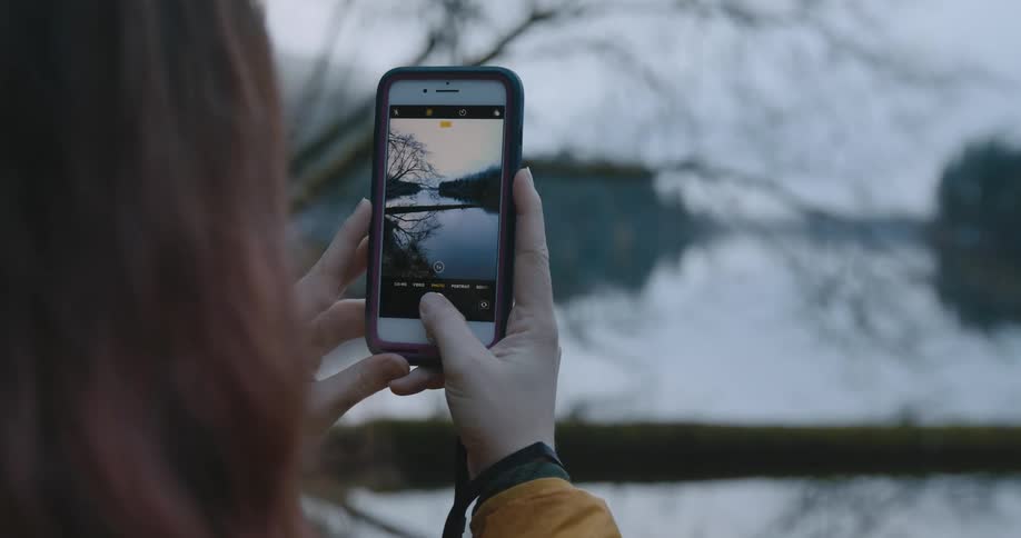 A woman holding up her phone taking a picture of a lake