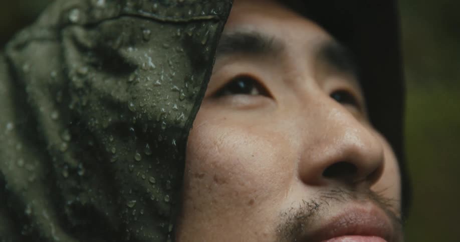 Rain falls on an asian man wearing a rain hat
