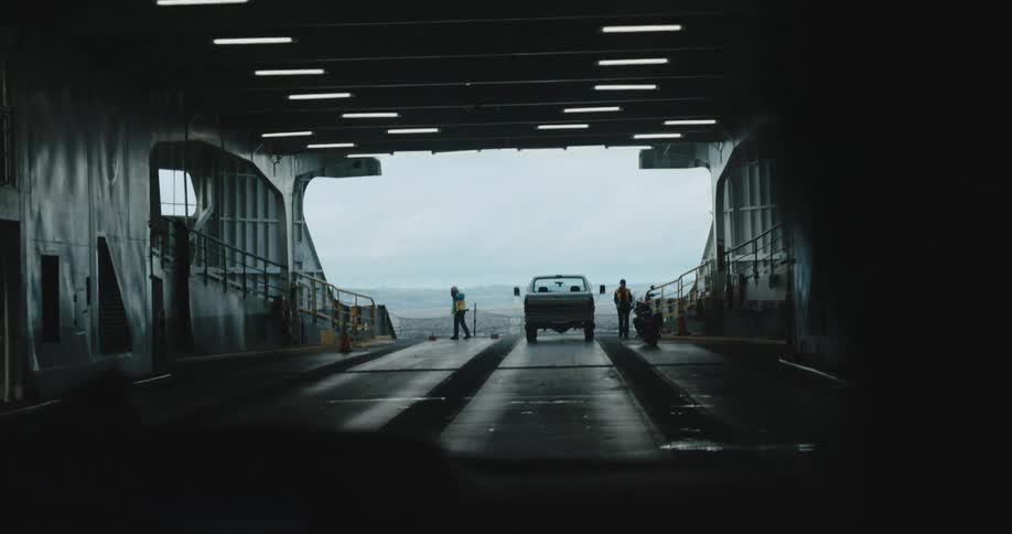 A person drives their vehicle onto a ferry towards workers and a parked pickup